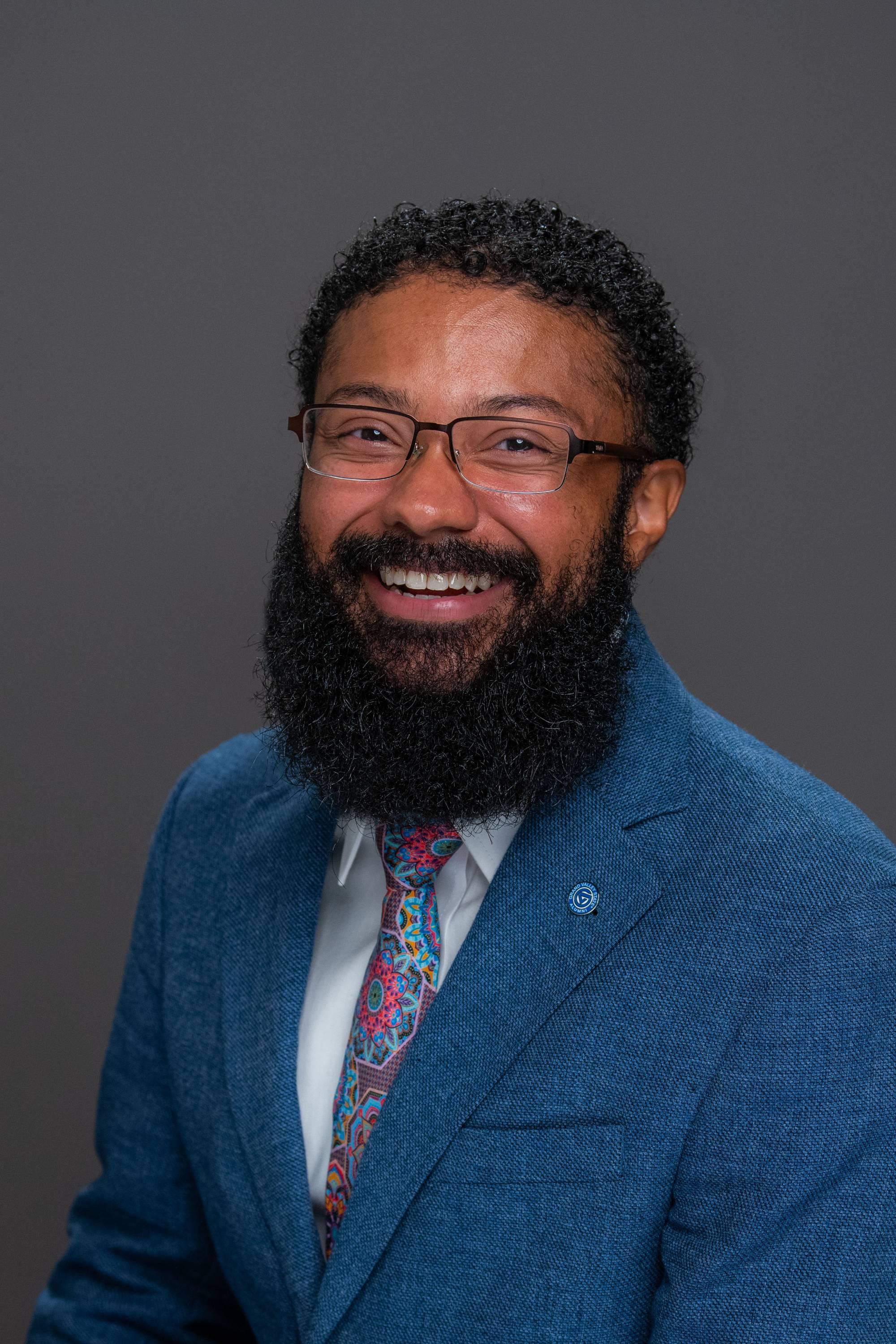 Ausar Martin wearing a blue shirt and gray suit jacket with a glass wall background
